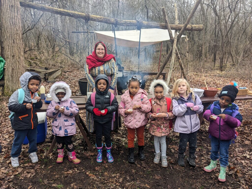 Children standing outside with coats on in front of a fire
